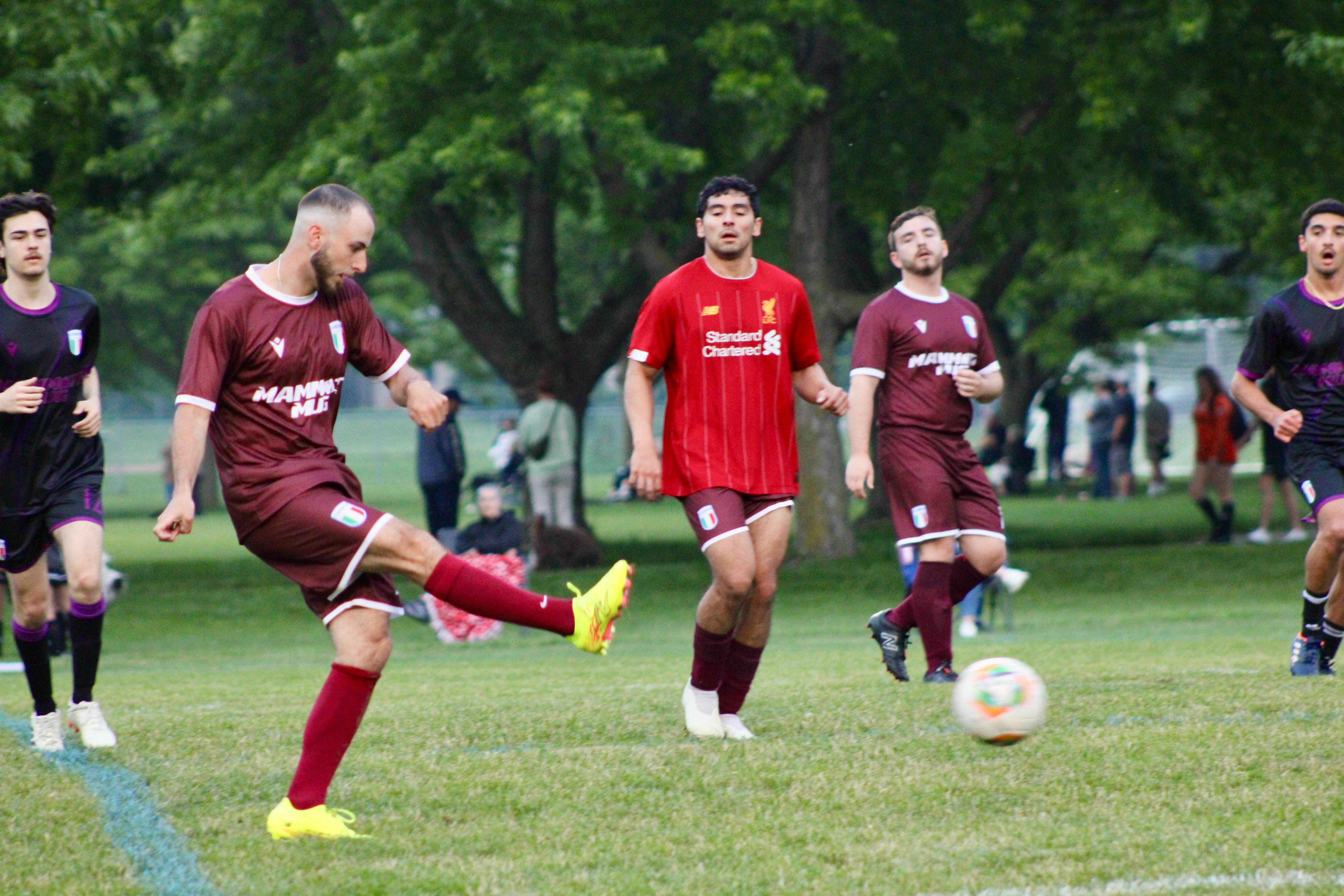 Buringa FC player taking a shot during outdoor match with teammates in maroon jerseys